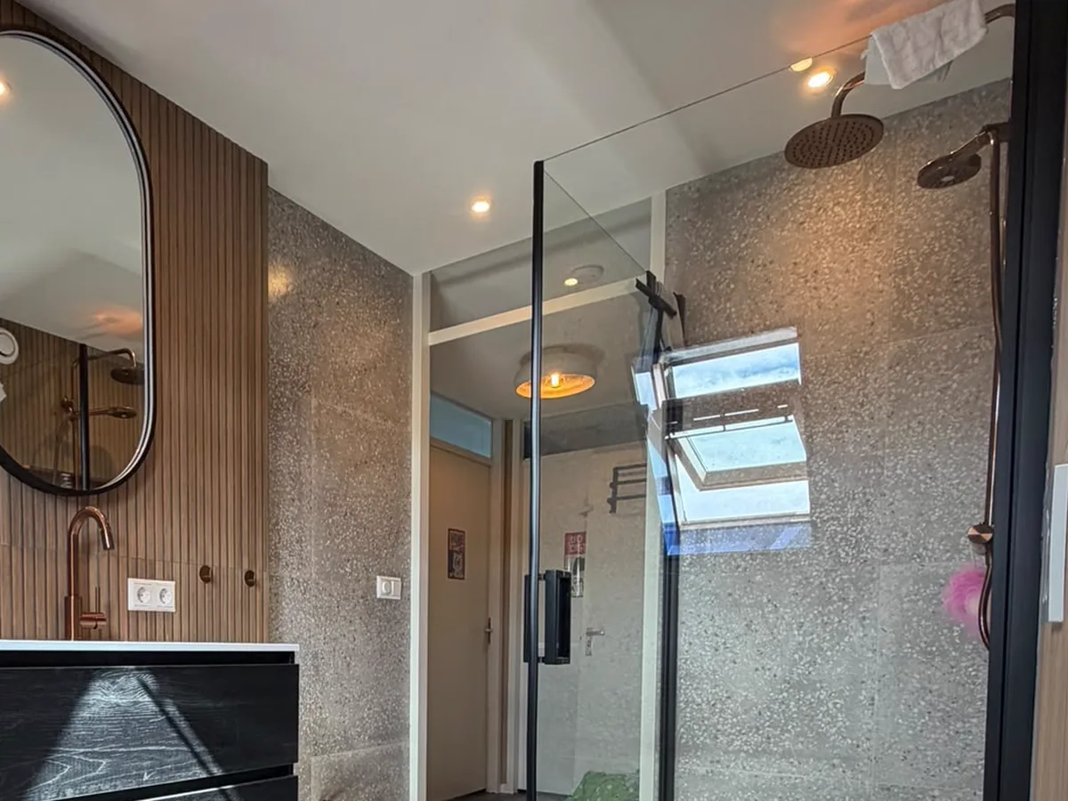 Opgeleverde badkamer met een inloopdouche in terrazzolook, een wand van houten lamellen en een zwart wastafelmeubel