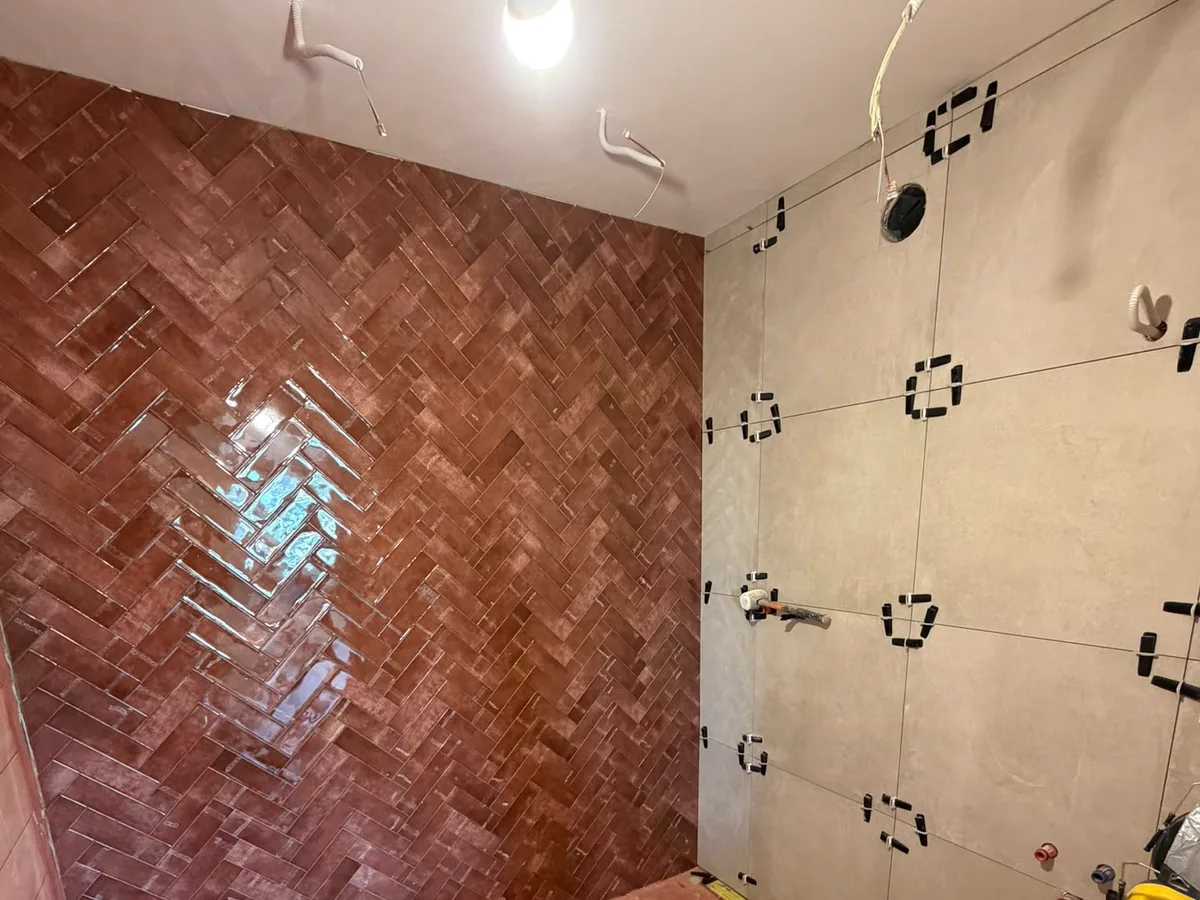 Wand in terracotta visgraattegels naast grootformaat wandtegels die nog gezet worden