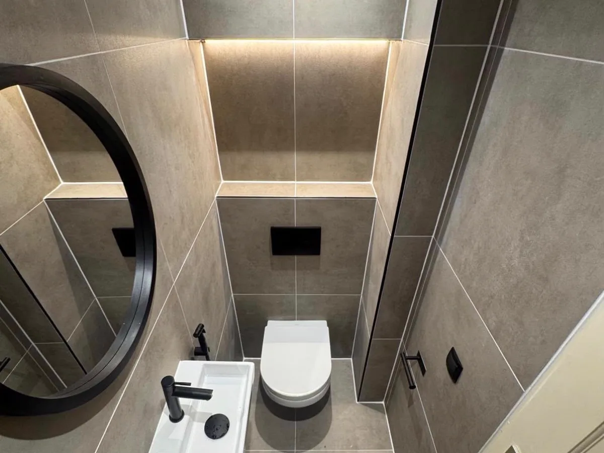 Opgeleverd toilet in betonlook tegels met een verlichte nis, hangtoilet en een ronde zwarte spiegel