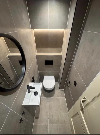 Opgeleverd toilet in betonlook tegels met een verlichte nis, hangtoilet en een ronde zwarte spiegel