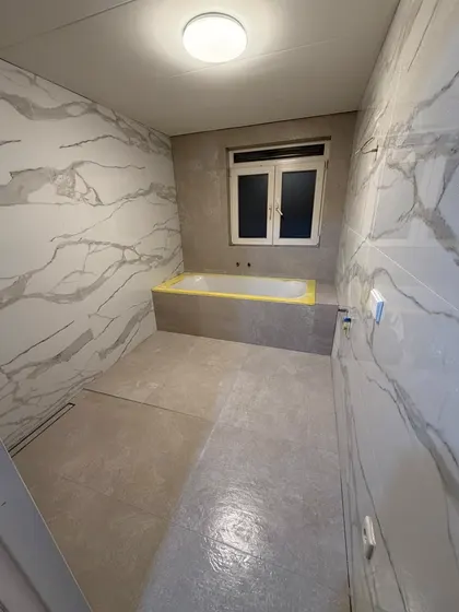 Badkamer met marmerlook wandplaten en een ingebouwd bad, de rand nog afgeplakt