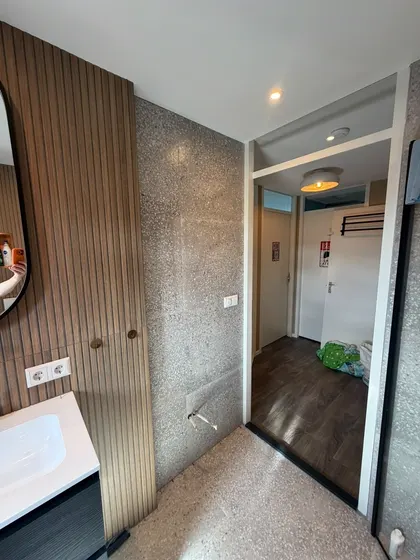 Badkamer met terrazzovloer, een wand in houten lamellen en zicht op de overloop